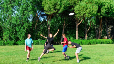 Group of mixed young teenagers people in casual wear playing with plastic flying disc game in a park oudoors. jumping woman catch a disk to a teammate