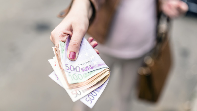 mana de femeie care intinde un teanc de euro