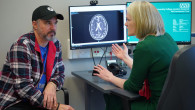 Medic vorbește cu pacientul în fața unui scan CT pe un monitor