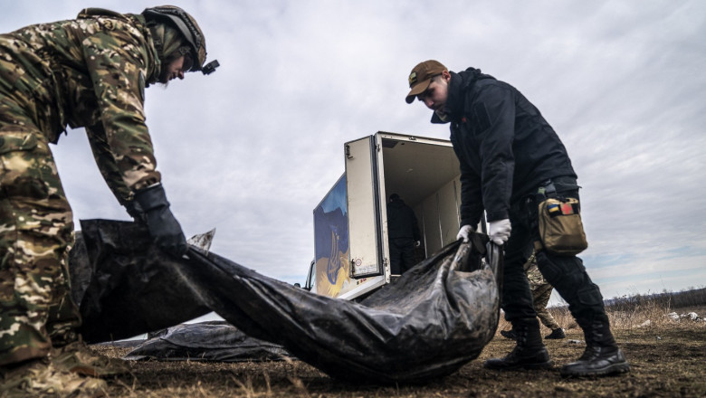 2 soldati ucraineni cara un sac cu cadavru de soldat rus