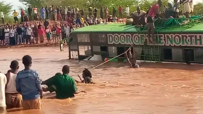 Passengers shelter on coach roof as vehicle is submerged while crossing a flooded bridge