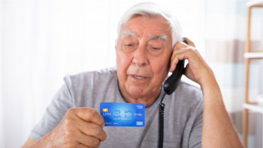 Bărbat vorbește la telefon cu cardul bancar în mână