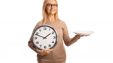 Woman holding a plate and a clock isolated on white background