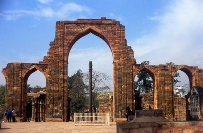 India: The remains of the Quwwat-ul-Islam Mosque and in the foreground the almost 2,000 year old Iron Pillar at the Qutb Minar complex, Delhi