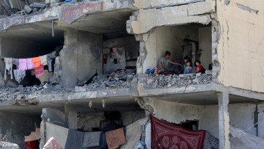 A Palestinian man and his children sit in a destroyed room following the targeting or a residential building by an Israeli airstrike in Rafah