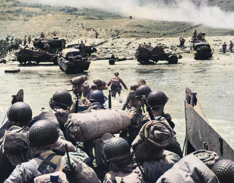 American assault troops prepare to disembark their landing craft as it approaches the beach head, Omaha Beach. The smoke visible in the background attests to the massive naval artillery assault, supporting the landing. Snakes of troops wind their way up t
