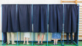 mai multe persoane voteaza in cabine de vot