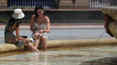 Two young women plunge their feet into the water of a fountain to cool off, in Plaza de Espana square in Sevill