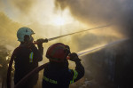 Athens, Greece. 19 June 2024. Firefighters attempt to extinguish a fire amidst thick smoke that has broke out in a factory area during a wildfire in the eastern suburbs of the Greek capital. Authorities have urged residents to evacuate an area on the frin
