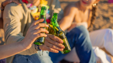 closeup three friends raise their green beer bottles in a toast against the backdrop of a stunning beach sunset. Their camaraderie shines through as t