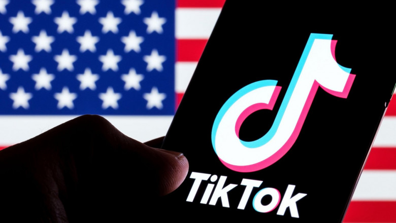 TikTok app logo seen on smartphone screen. U.S. US flag o the blurred background. Stafford, UK, February 28, 2023