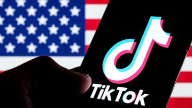 TikTok app logo seen on smartphone screen. U.S. US flag o the blurred background. Stafford, UK, February 28, 2023