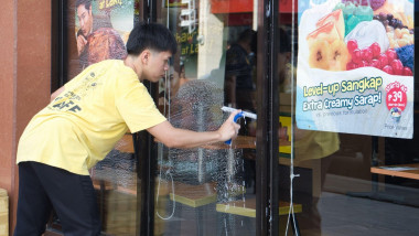 A man in a yellow shirt is cleaning a window. The window is covered in streaks and the man is using a squeegee to clean it