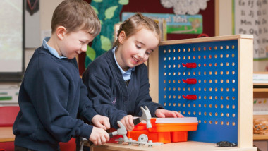 Pupils in school uniform at a Primary School in the UK playing with toy hand tools.