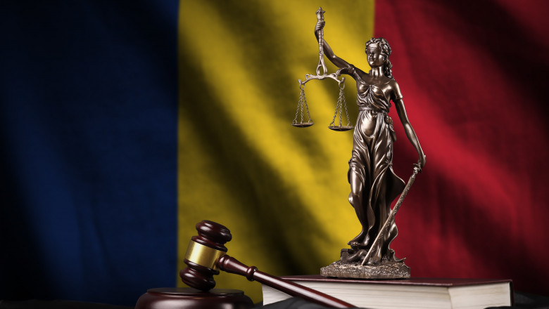 Romania flag with statue of lady justice, constitution and judge hammer on black drapery. Concept of judgement and guilt