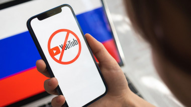 Poltava, Ukraine - March 23, 2022: Woman try to use Youtube in Russia. Smartphone with banned logo of Youtube and Russian flag background