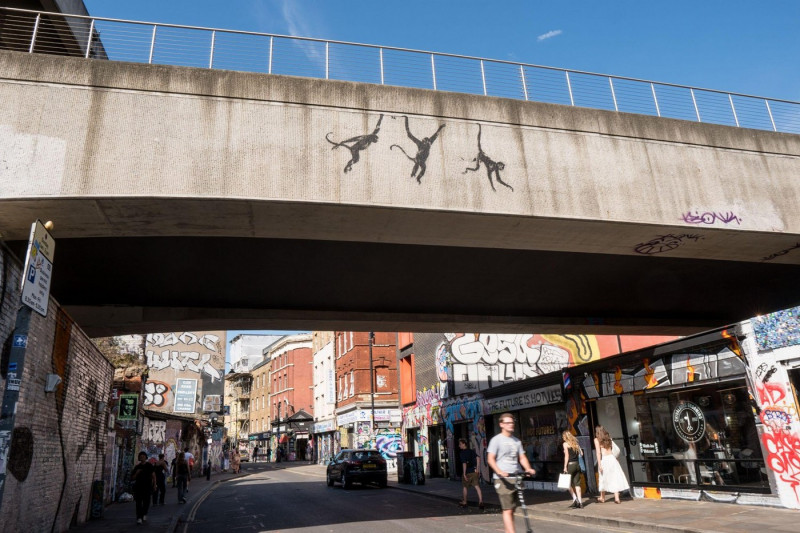 Banksy three swinging monkeys on railway bridge Brick Lane in Shoreditch London, 13th August 2024, part of his zoo collection