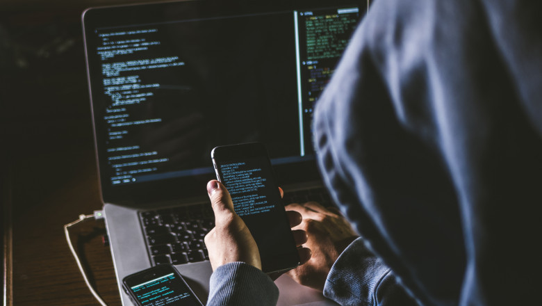 hacker la computer, cu un telefon in mana