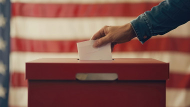 Election in USA. Man's hand putting his vote in the ballot box. American flag on background