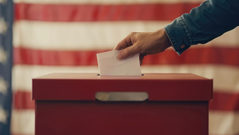 Election in USA. Man's hand putting his vote in the ballot box. American flag on background