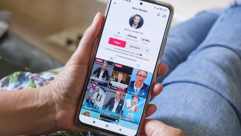 Frau hält ein Mobiltelefon auf dessen Display die Seite der AFD Politikerin Alice Weidel auf Plattform TikTok zu sehen i