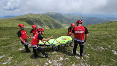 4 salvamontisti duc o targa pe roti pe munte, cu pacient ranit