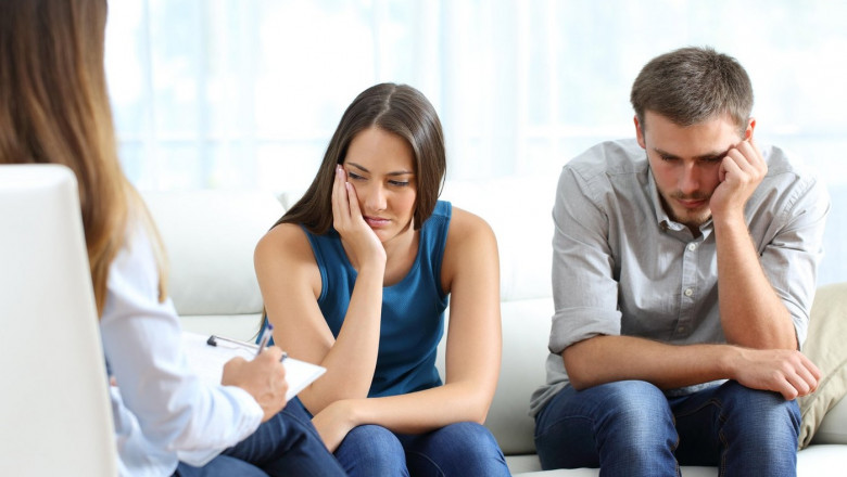 Sad couple listening to a marriage counselor during a therapy sitting on a sofa at home