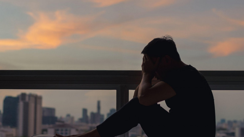 A person sitting and feeling depressed on bed with city view in dusk moment. Stay home, depression and loneliness concept.