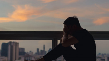 A person sitting and feeling depressed on bed with city view in dusk moment. Stay home, depression and loneliness concept.