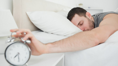 Sleeping handsome man being awakened by an alarm clock