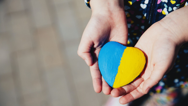 Small little kid hold heart shaped stone with Ukraine national flag or anthem