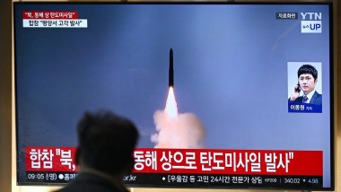 A man watches a television screen showing a news broadcast with file footage of a North Korean missile test,