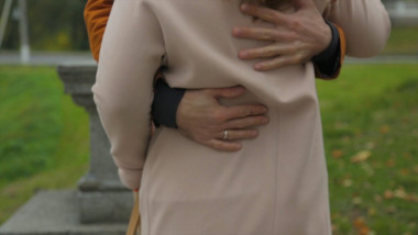 Couple standing on street and hugging. Man hugs a woman view from the back. Closeup of woman hands hugging man outside