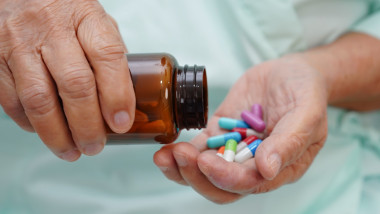 Asian elderly woman holding pill capsule drug in hand.