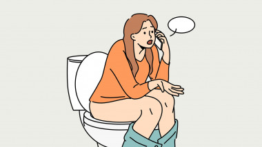 Woman sits on toilet bowl in toilet and talks on phone with friend, discussing colleagues from work