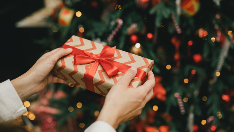 Young,Woman,Holding,Wrapped,Christmas,Present,With,A,Red,Ribbon,