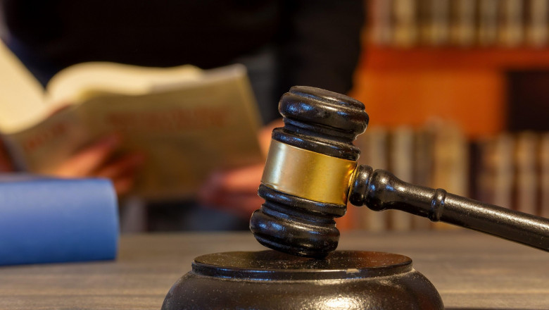 Close-up of a judges gavel, in the background a man reads a law book (symbol image)