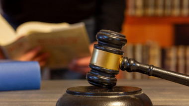 Close-up of a judges gavel, in the background a man reads a law book (symbol image)