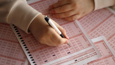 Filling out a lottery ticket. A young woman plays the lottery and dreams of winning the jackpot. Female hand marking number on red lottery ticket