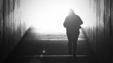 Black and white image of a single solo alone woman fading away, walking towards a bright light at the end of a tunnel. Suicide, death dying lost loved