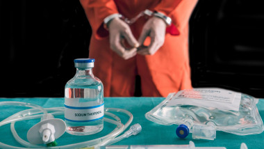 Prisoner handcuffed to death by lethal injection, vial with sodium thiopental and syringe on top of a table, conceptual image