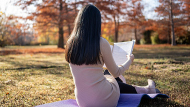 Woman enjoying reading a book while sitting on a yoga mat in a peaceful autumn park