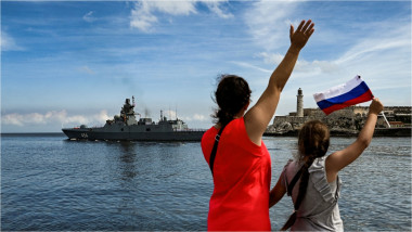 O femeie și o fată din Cuba care flutură steagul Rusiei salută o navă rusească venită în portul din Havana