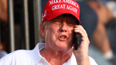 Trump cu șapcă roșie MAGA pe cap vorbește la telefon