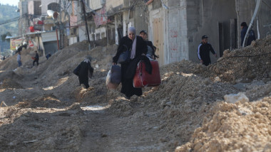 People carry their belongings as they cross a destroyed street while fleeing the Nur Shams camp