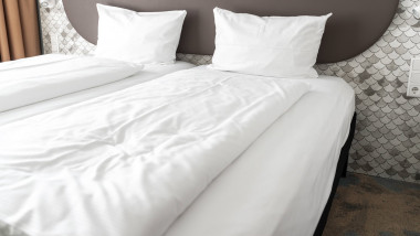 8 July 2023: Bed in hotel room with white comforter and white pillows *** Bett in einem Hotelzimmer mit weißer Bettdecke