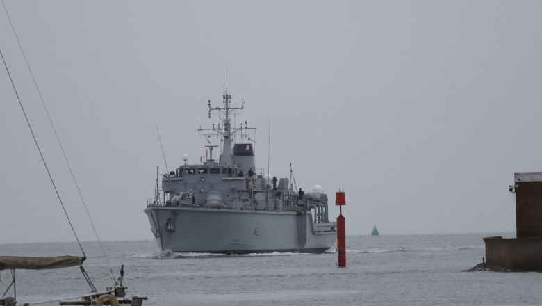 At the mouth of the harbour, passing a red marker: HMS Cattistock, a Royal Navy Hunt Class minesweeper returns to her home base, Portsmouth, after having been involved in a week-long operation to monitor two Russian Navy task groups passing the UK, worki