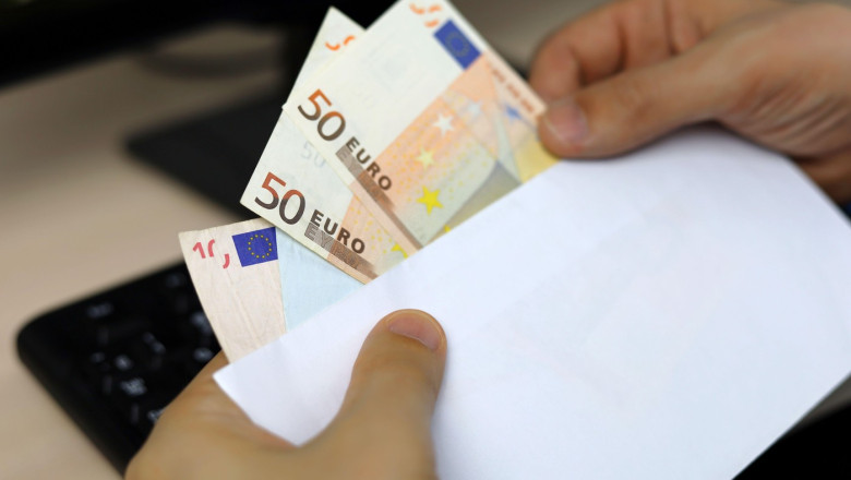 Envelope with euro banknotes in male hands. Man pulls money out of an envelope on PC keyboard background, wages, bonus or bribe concept