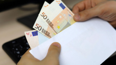 Envelope with euro banknotes in male hands. Man pulls money out of an envelope on PC keyboard background, wages, bonus or bribe concept