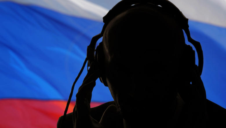 Silhouette of a man wearing headphones, eavesdropping secret agent, spy and scout, Russian flag, backlight.